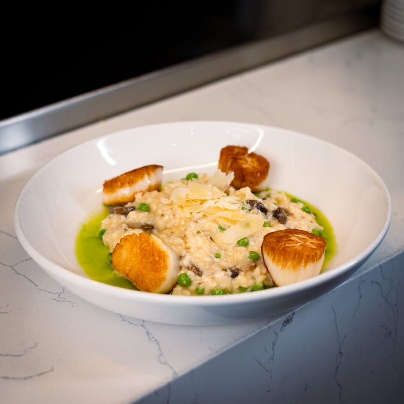 Creamy Italian risotto with peas, mushrooms, parmesan, and seared scallops in a white bowl.