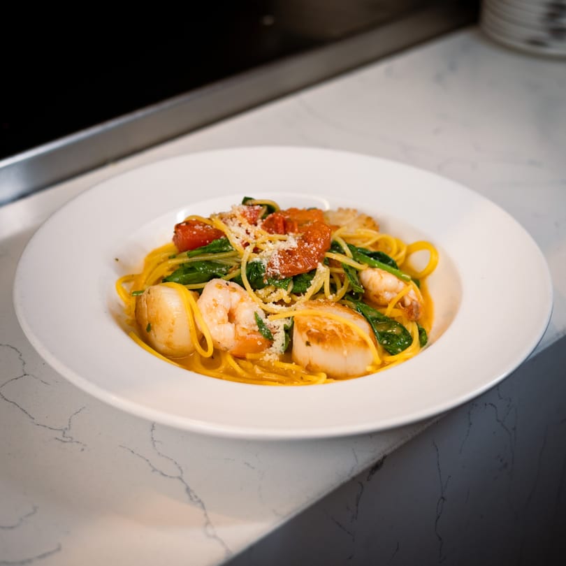 Cucina Colore's seafood pasta with scallops, shrimp, spinach, and tomatoes, topped with parmesan.