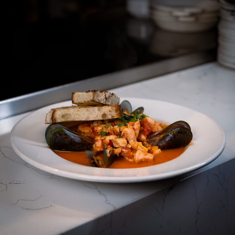 Cucina Colore's Italian seafood stew with mussels, fish, and crusty bread on a white plate.